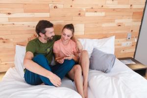 Ein Mann und eine Frau sitzen auf einem Bett und sehen auf ein Handy. in der Unterkunft JUFA Alpenhotel Saalbach in Saalbach-Hinterglemm