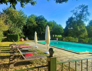 a swimming pool with two umbrellas next to a fence at LA CHARMILLE Jolie maison de campagne 14 personnes piscine calme in Entrains-sur-Nohain