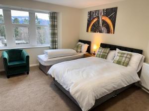 a bedroom with two beds and a chair and windows at Forces Manor in Kincraig