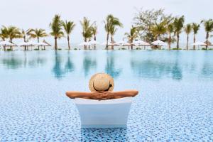 a person in a straw hat sitting in a chair next to a pool at Mövenpick Resort Waverly Phu Quoc in Phu Quoc
