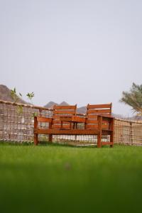two wooden benches sitting in the grass near a fence at Dibba Mountain Park Resort in Fujairah