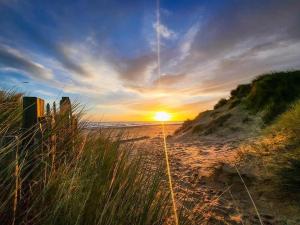 a sunset over a beach with grass and the ocean at Chalet 145, Hemsby - Two bed chalet, sleeps 5, pet friendly, bed linen and towels included and close to beach! in Great Yarmouth +5 photos