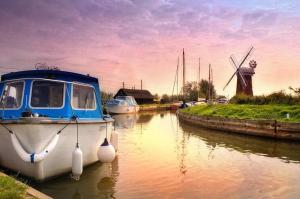 a boat is docked in a canal with a windmill at 194, Belle Aire, Hemsby - Two bed recently renovated chalet, sleeps 4, pet friendly, free Wi-Fi and bed linen and towels included in Hemsby