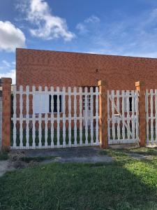 einen weißen Zaun vor einem Backsteingebäude in der Unterkunft Casa com 2 quartos grandes a 150m da praia in Rio Grande