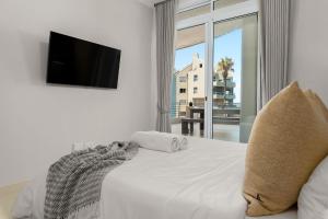 a bedroom with a white bed with a flat screen tv at Portico in Bloubergstrand