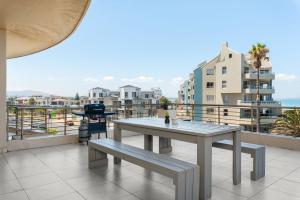 a table and bench on a balcony with buildings at Portico in Bloubergstrand