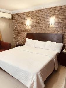 - une chambre avec un grand lit blanc et un mur en briques dans l'établissement BELIANA SUITES, à Uyo