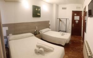 Dos camas en una habitación con toallas blancas. en Hostal Nevot en Granada