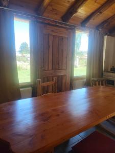 a large wooden table in a room with two windows at Complejo Turístico PET Friendly Los Abuelos- Cabaña ENCANTO NATURAL. in Cholila