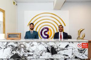 Dos hombres de traje sentados detrás de una mesa con un objetivo. en Click Sunburry Hotel Srinagar, en Srinagar