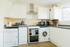 Una cocina con gabinetes blancos y lavadora y secadora. en Canterbury 3BR close to shops with Free Parking, en Kent