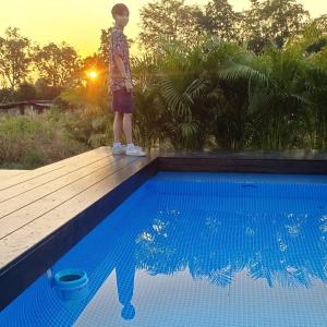 a boy standing on a deck next to a swimming pool at Baannoi in the garden บ้านน้อยกลางทุ่งpool villa 