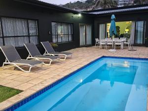 una piscina con sillas, una mesa y un patio en Angel Bay, 129 Nkwazi Drive, Zinkwazi, en Zinkwazi Beach
