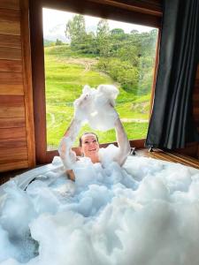 a man laying in a cloud bath tub with a window at Chalé Vista Das Araucárias in Urubici