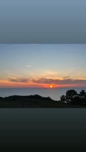 a sunset over the ocean with trees in the foreground at Hotel Restaurante el Fornon in Novellana
