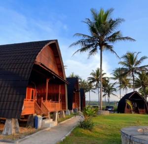 a building with a palm tree next to a field at Palma Beach Resort in Padangnegeri