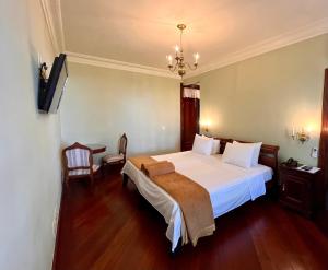sypialnia z dużym białym łóżkiem i żyrandolem w obiekcie Aroso Paço Hotel w mieście Pedra Azul