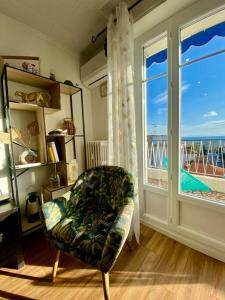 ein Wohnzimmer mit einem Stuhl und einem großen Fenster in der Unterkunft Nice 2P Vue Mer- 5min plage, Terrasse, AC, Parking in Nizza