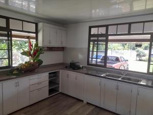 Fare Tetahora في Tevaitoa: مطبخ بدولاب بيضاء ومغسلة ونوافذ