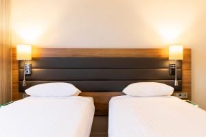 two beds in a hotel room with white sheets at Moxy Aberdeen Airport in Dyce