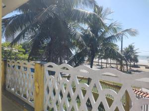 uma cerca branca em frente a uma praia com palmeiras em Pousada em Mongaguà Kali 2 em Mongaguá