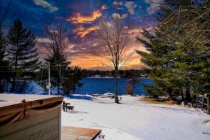 una puesta de sol sobre un lago con nieve y árboles en Zen Den - Pocono LakeFront with Hot Tub !, en Pocono Summit