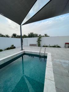 a swimming pool with a umbrella and a patio at نزل الغيم -Cloudinn in Qārūt al ‘Ulyā