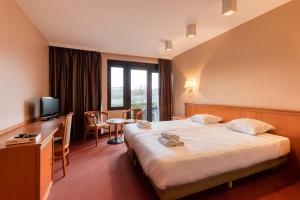 a hotel room with a bed and a desk and a television at Corsendonk Duinse Polders in Blankenberge