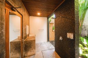 a bathroom with a shower with a stone wall at The Farm Hostel in Canggu