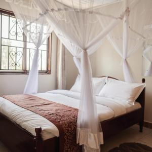 a bedroom with a canopy bed with white drapes at Acacia Country Inn in Mbarara