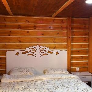 a bedroom with a white bed with a wooden wall at الكوخ الريفي in Al Majma'ah