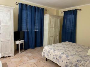 Schlafzimmer mit blauen Vorhängen, einem Bett und einem TV in der Unterkunft Hotel Villa Del Parco in La Maddalena