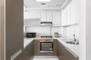 a white kitchen with a sink and a stove at Nasma Luxury Stays - Sleek City Haven 1BR in Dubai's Glitz Residence 3 in Dubai