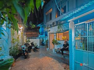 une femme assise sur un banc devant un bâtiment bleu dans l'établissement 8h-hostel, à Hô-Chi-Minh-Ville