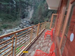 een rode stoel op een balkon met een waterval bij Red House Cafe & Inn in Jibhi