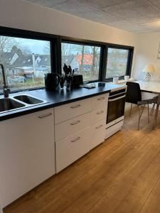 a kitchen with white cabinets and a sink and windows at Den gammel togstation in Give