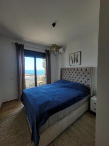 a bedroom with a bed with a blue comforter and a window at SeaView Apartment & Pool in Ulcinj