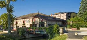 um edifício ao lado de um rio com um edifício em L'Escale Ocre - 150m Restaurant 3 étoiles em Vonnas