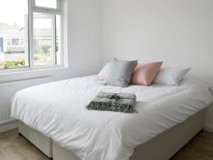 a white bed with white sheets and pillows and a window at Swallows Nest in Bude