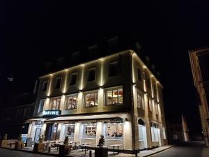 un bâtiment éclairé avec des tables à l'extérieur la nuit dans l'établissement Le Grand Hôtel de la Marine, à Port-en-Bessin-Huppain