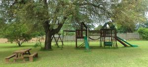 a playground in a park with a tree and a bench at Sand River Cottages in Hazyview