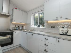 a white kitchen with white cabinets and a window at Bluebell Lodge in Dartmouth