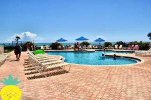 una piscina con tumbonas y sombrillas azules en "SHERWIN" Coastal Vibes Oceanfront Condominiums en Daytona Beach