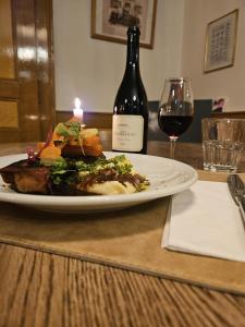 einen Teller mit Essen, eine Kerze und eine Flasche Wein in der Unterkunft Hôtel Von Bergen in La Sagne