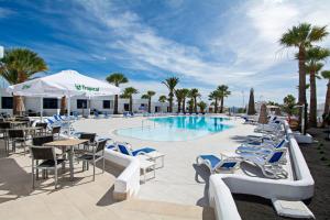 una piscina con mesas, palmeras y sillas azules y blancas en Apartamentos Panorama Adults Only en Puerto del Carmen