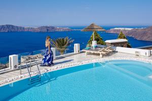 una mujer con un vestido azul de pie junto a una piscina en Santorini Princess Spa Hotel en Imerovigli