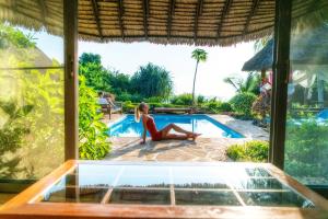 Eine Frau in einem roten Bikini sitzt neben einem Pool. in der Unterkunft Zanzi Resort in Zanzibar City