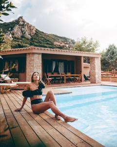 Eine Frau im Bikini, die auf einem Deck neben einem Pool sitzt. in der Unterkunft Costa Paradiso Resort in Costa Paradiso