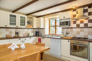 uma cozinha com armários brancos e uma mesa de madeira em Mill Cottage - Great Houndbeare Farm Holiday Cottages em Aylesbeare