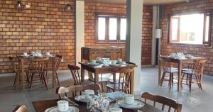 Pousada dos Cânticos في Barra: غرفة طعام مع طاولات وكراسي وجدار من الطوب